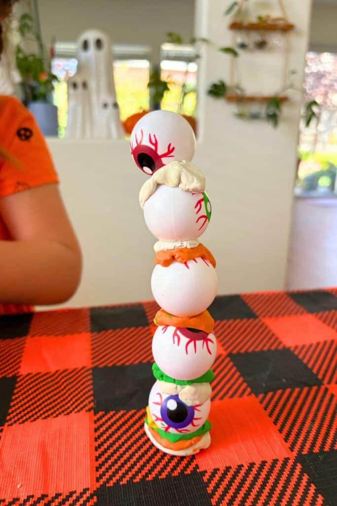 A five-ball eyeball tower for this Halloween STEM activity, stacked with alternating layers of white, orange, and green clay.
