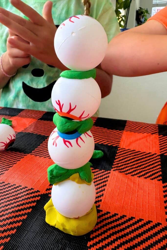 Close-up of a four-ball eyeball tower being carefully balanced, with green and blue clay layers holding each eyeball in plac