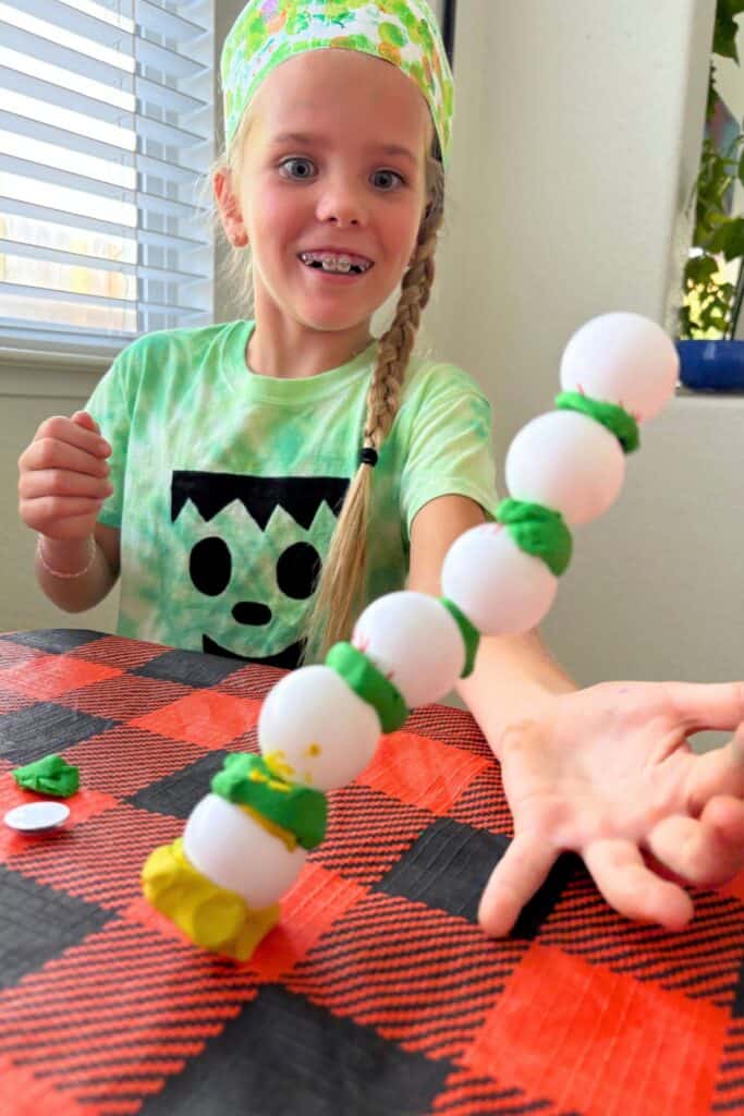 A girl holding up her eyeball tower sideways to show off the full stack of clay and eyeball layers before it comes apart.