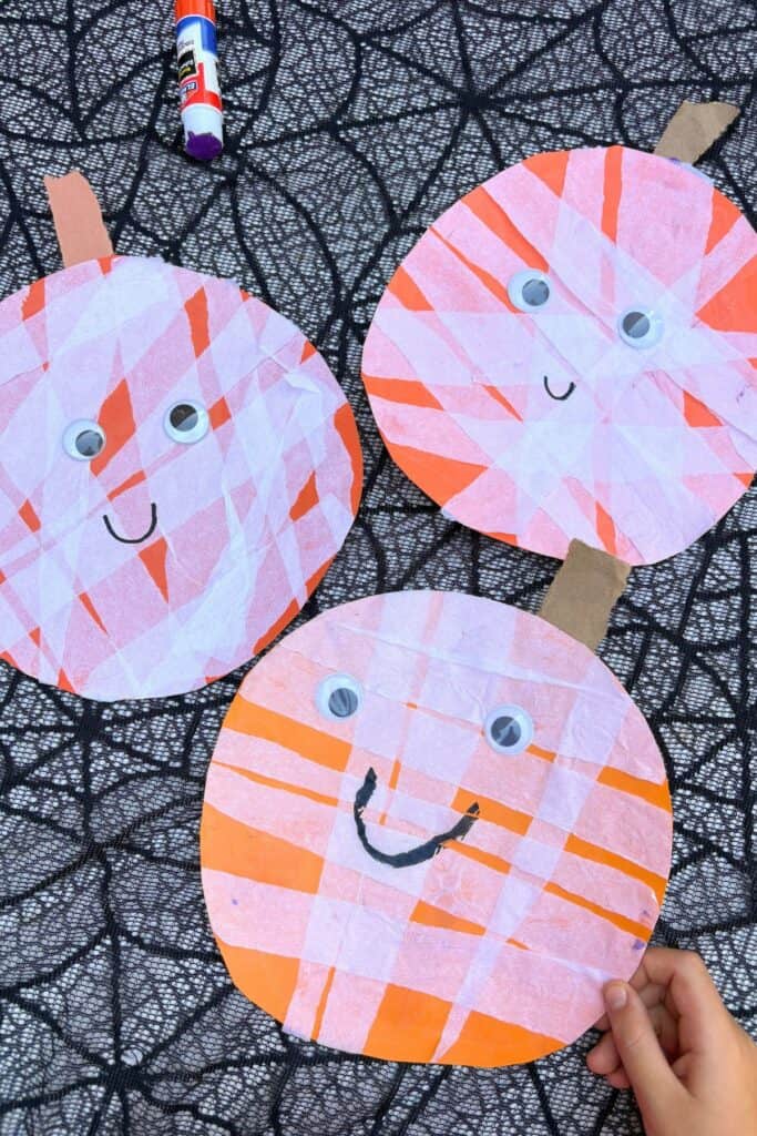 Child holding a finished mummy pumpkin craft with white tissue paper strips, googly eyes, and a cardboard stem.
