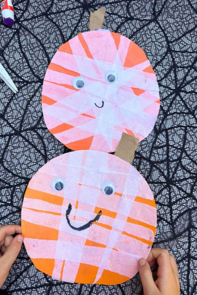 Finished jack-o-lantern craft for Halloween pumpkins with white tissue paper, googly eyes, orange paper bases, and cardboard stems.