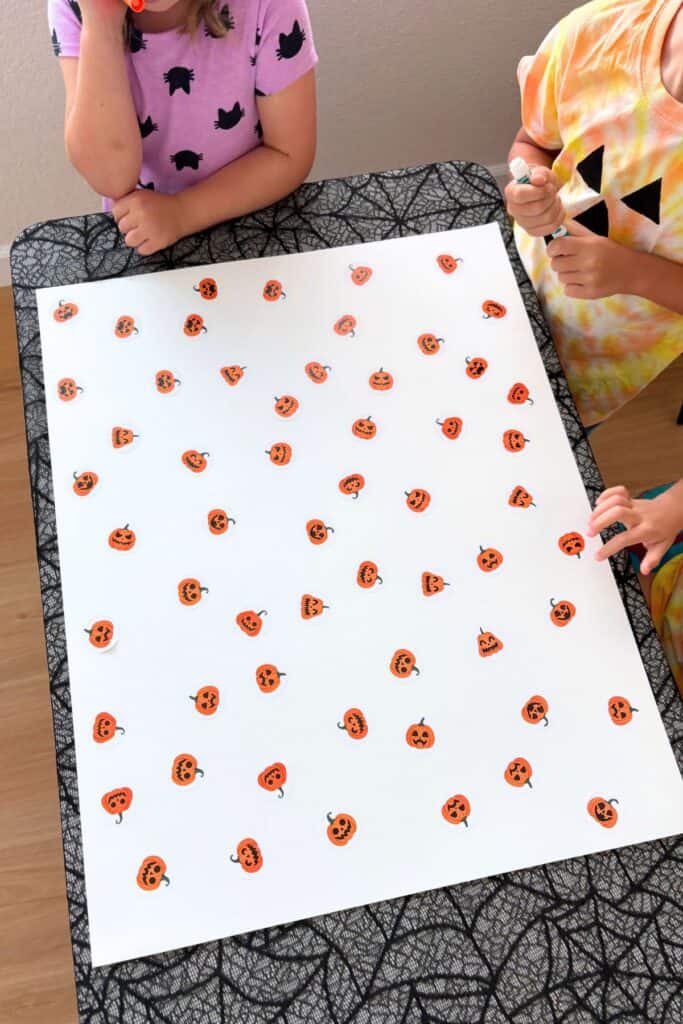Kids getting ready for a preschool Halloween activity with matching jack-o-lantern stickers arranged on a large sheet of white paper.
