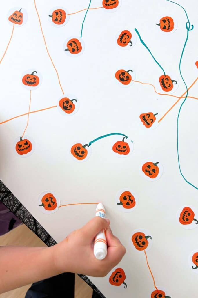 Close-up of a preschool Halloween activity with colorful marker lines connecting matching jack-o-lantern stickers.
