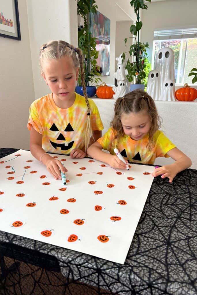 Two children drawing lines between matching pumpkin stickers during a preschool Halloween activity.